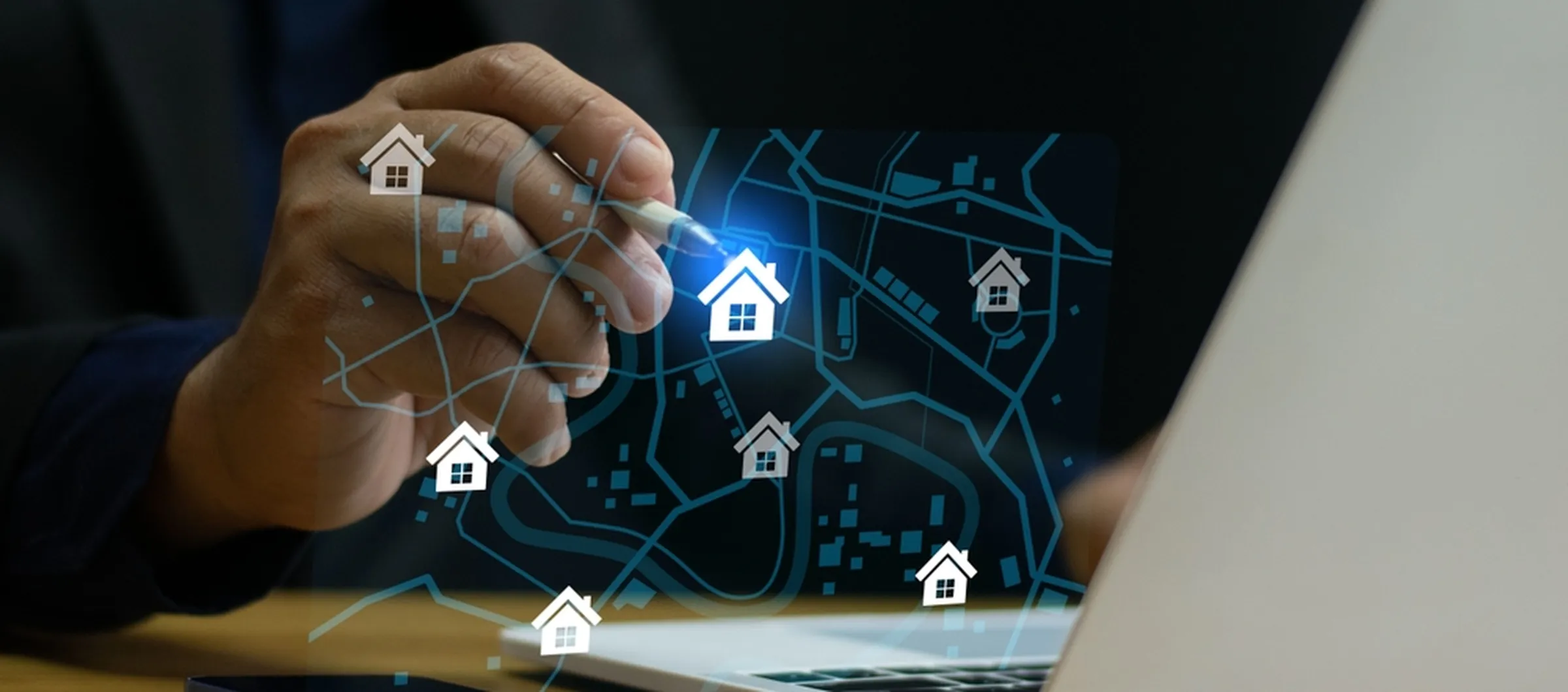 Persona utilizando un lápiz óptico en un portátil que muestra un mapa digital con iconos de casas, que simboliza la búsqueda inmobiliaria en línea o la gestión de fincas.